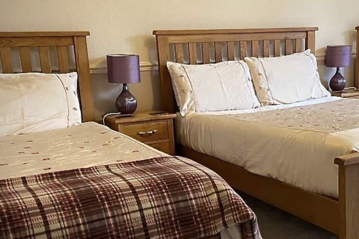 Um quarto com três camas de madeira, cada uma com uma mesa de cabeceira e uma luminária.