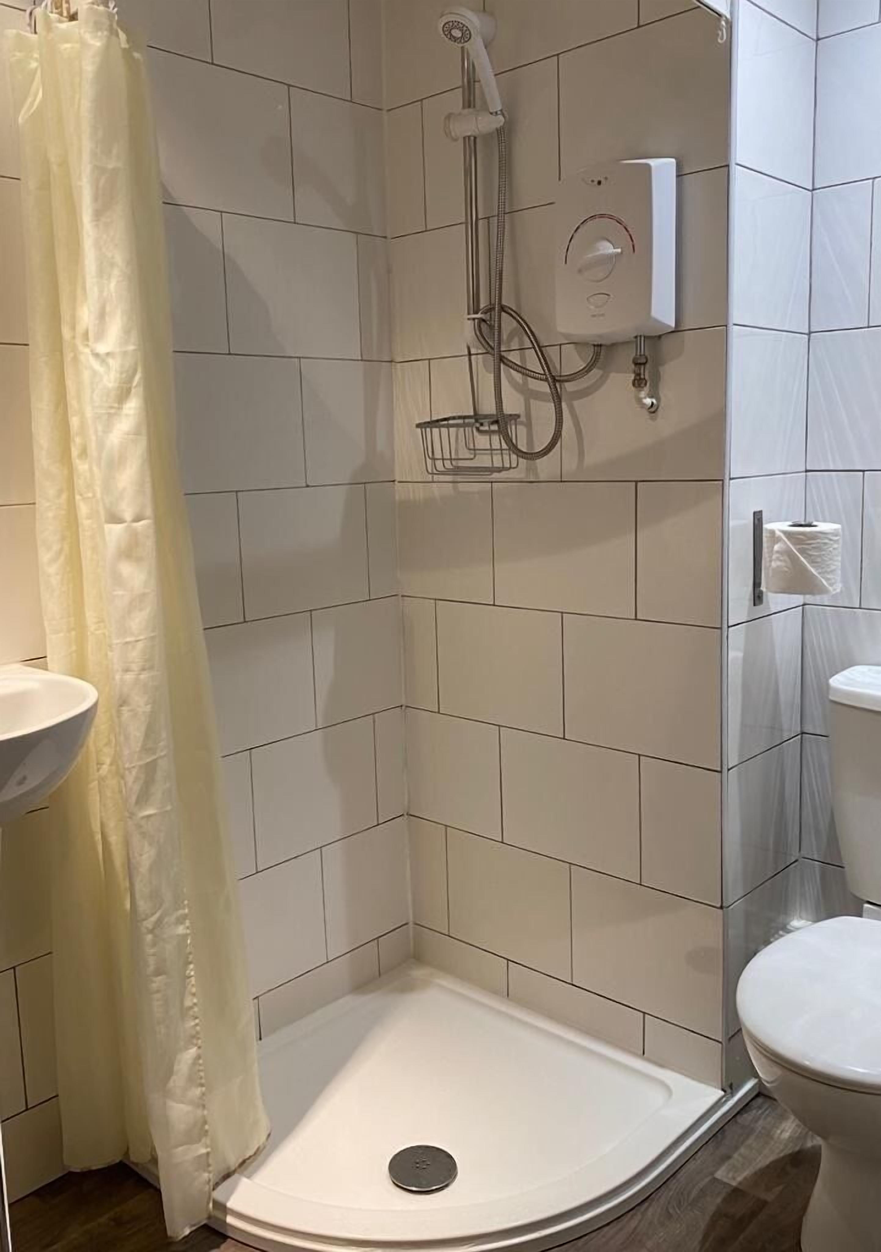Une salle de bain avec des carreaux blancs, une douche, des toilettes et un lavabo.