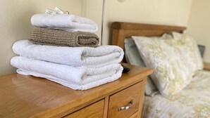 Une table de chevet en bois, sur laquelle sont pliées plusieurs serviettes, et une lampe.