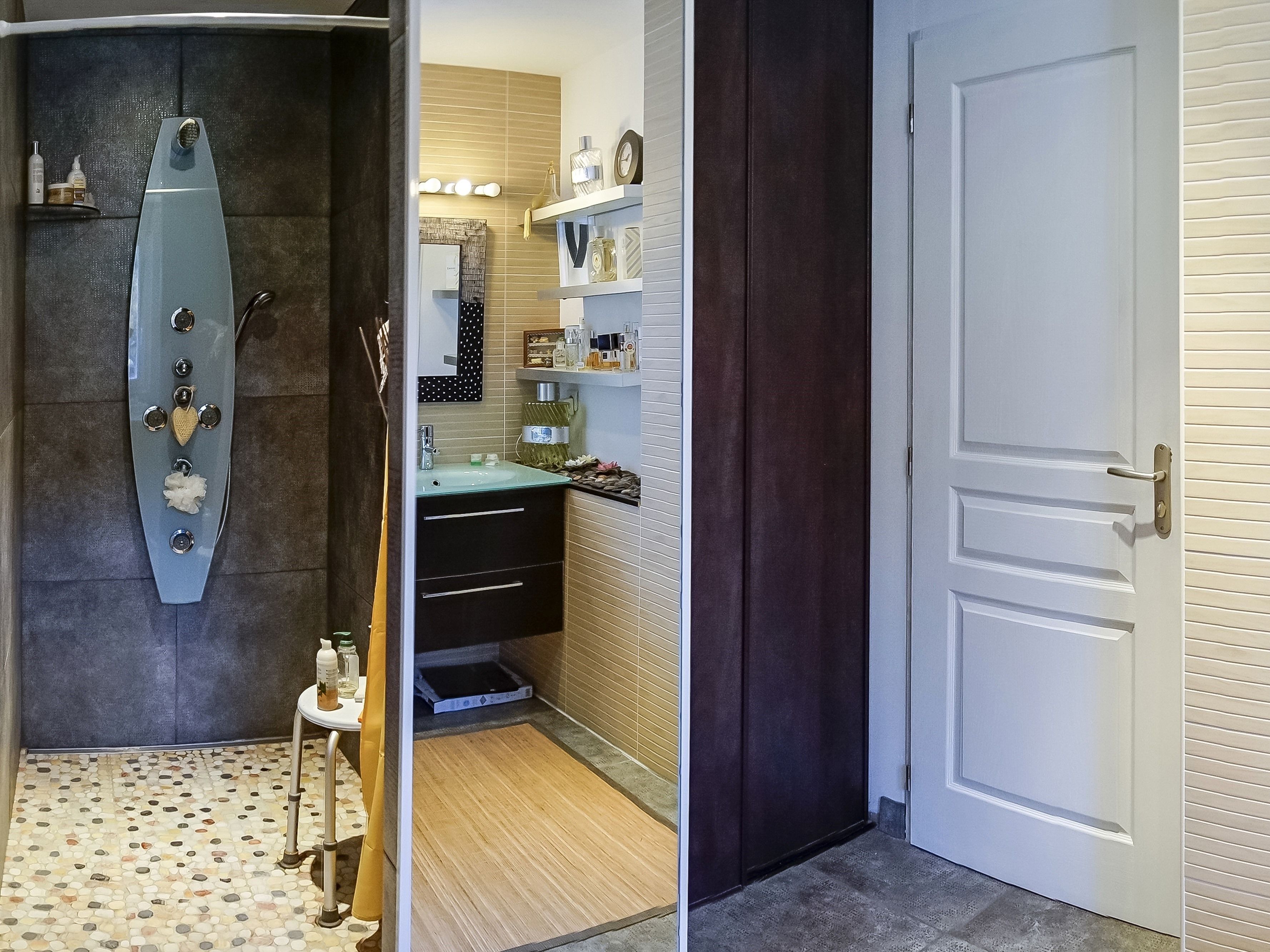 A bathroom with a modern shower, a vanity with a mirror, and a door leading to another room.