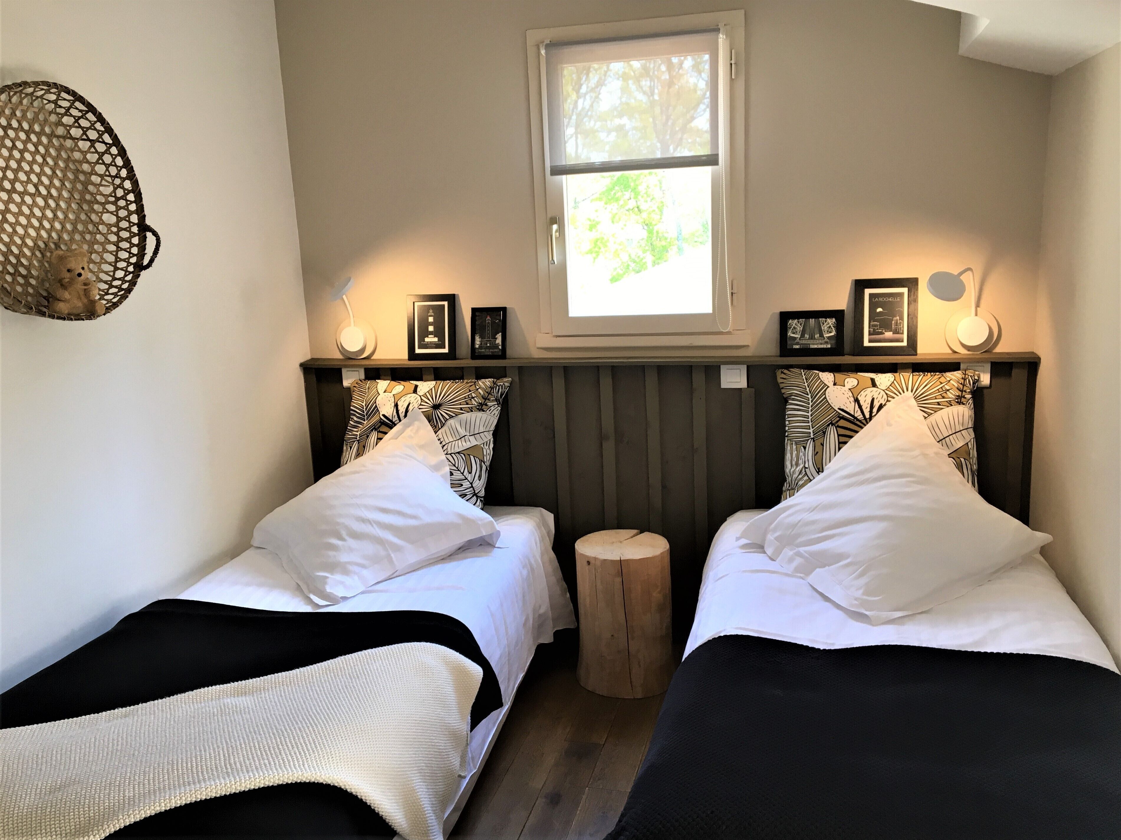 Une chambre avec deux lits, une fenêtre et un tabouret en bois.
