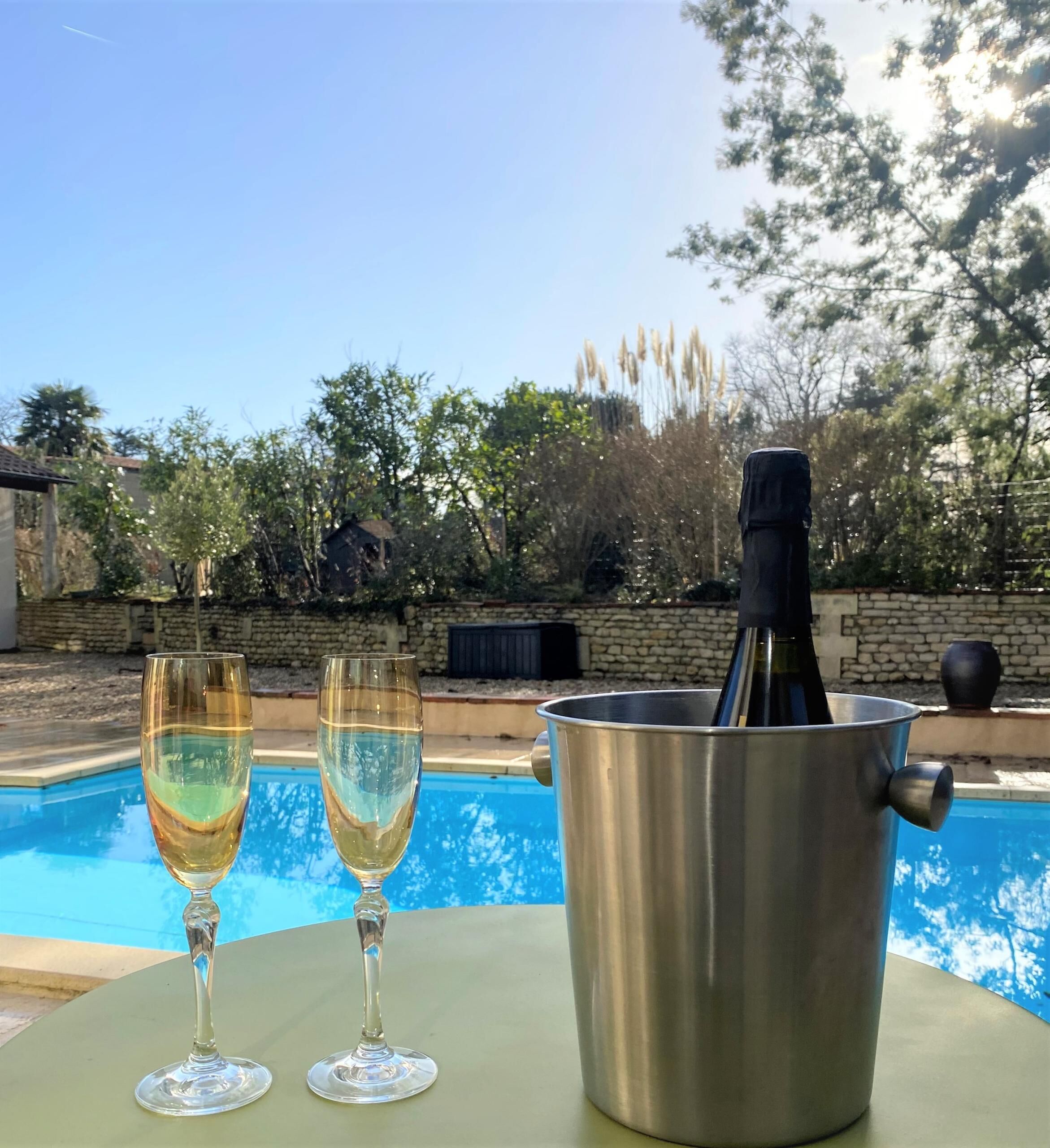 En miljö vid poolen med två glas vitt vin och en flaska i en metallhink.