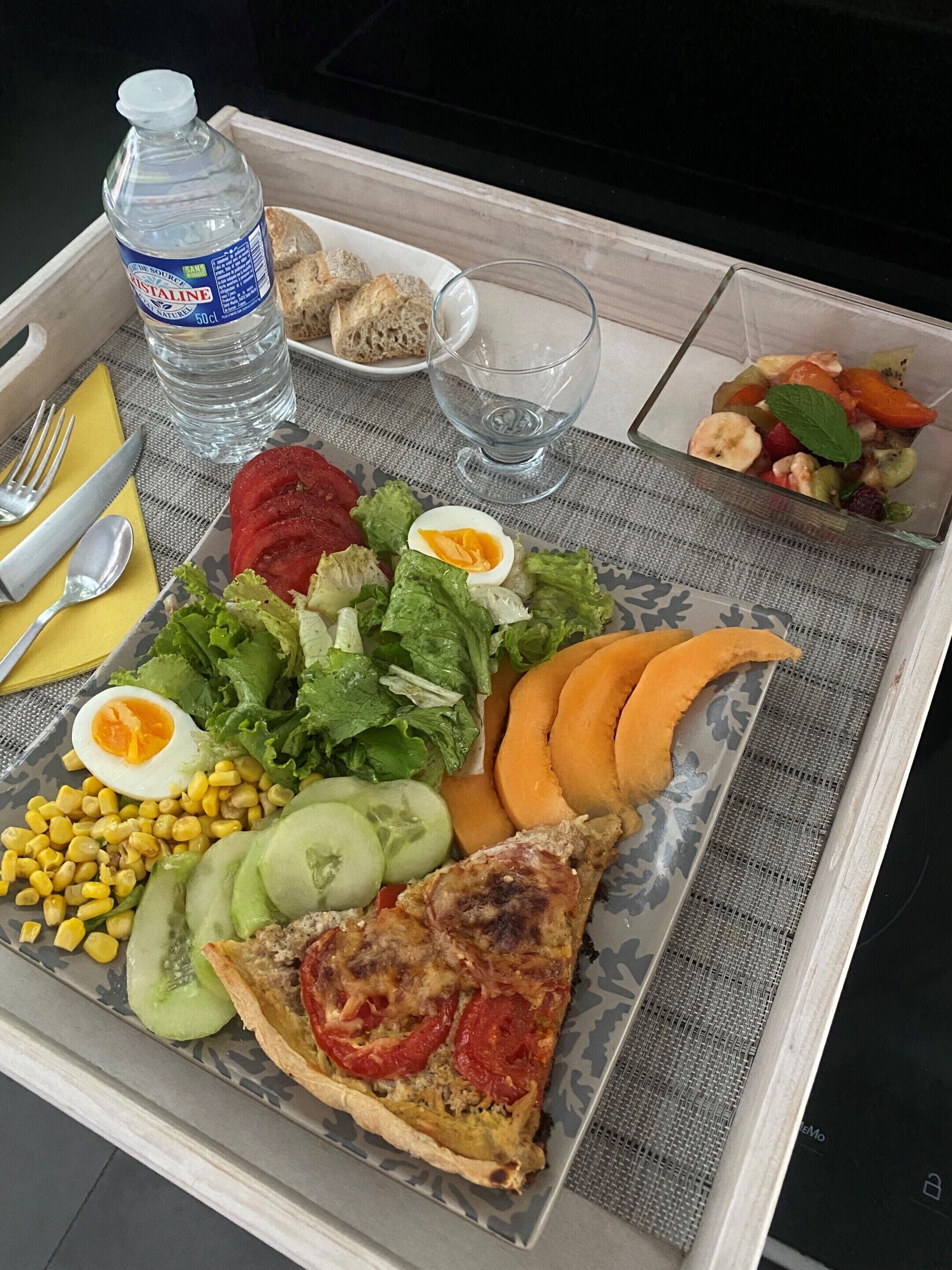 A plat amb diverses menes de menjar, incloent una làmina de pizza, amanida de lletuga, tomàquets, blat de moro i un ou dur.