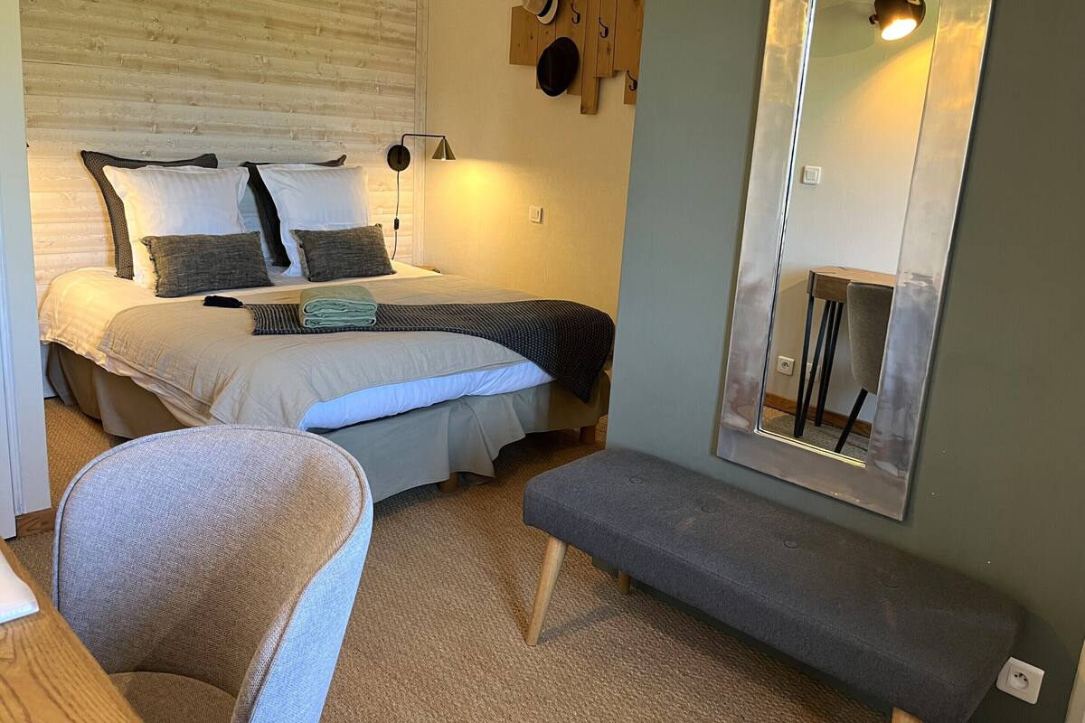 A bedroom with a bed, bedside table, chair, bench, and a mirror.