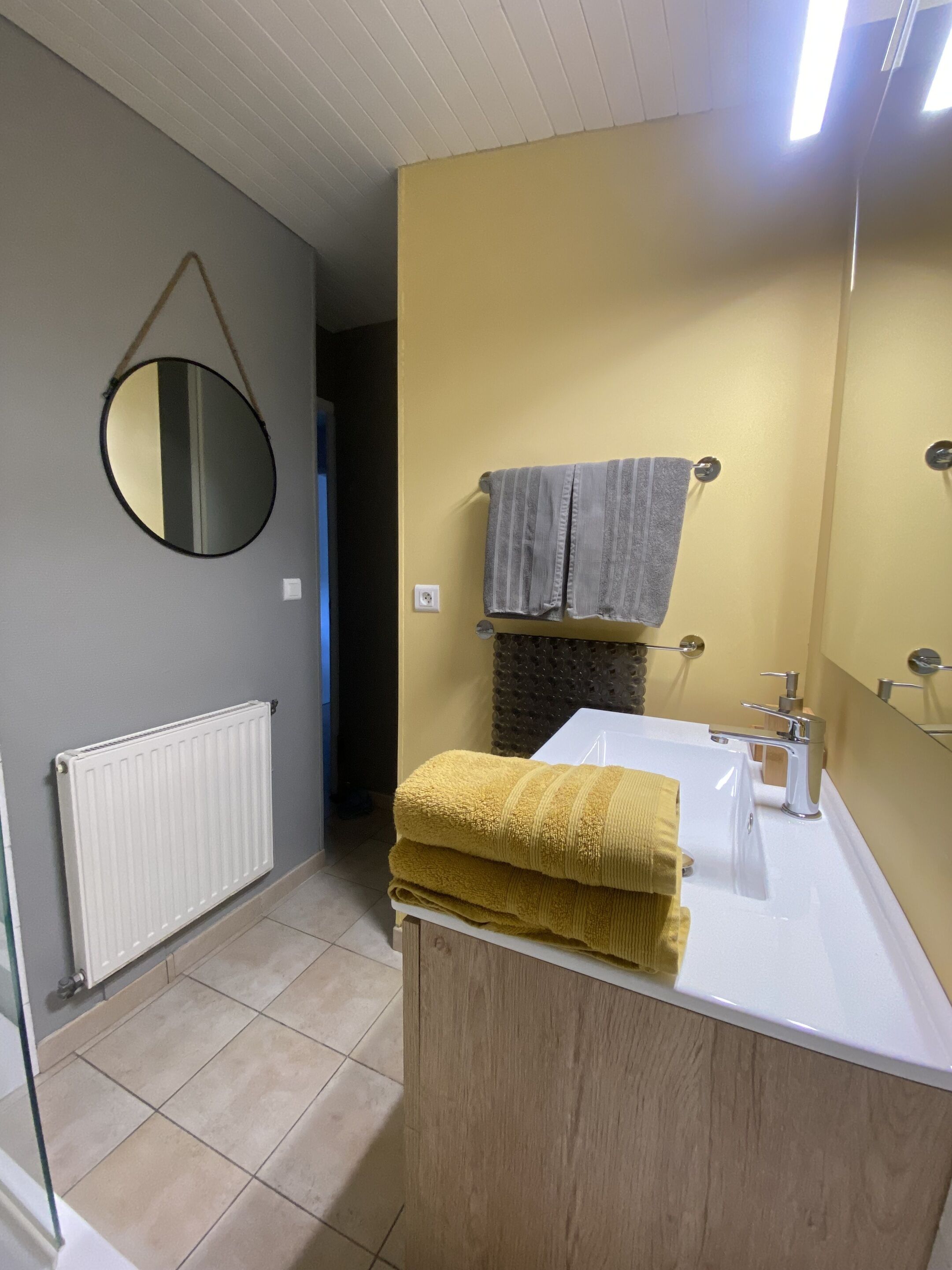 Un baño con un lavabo blanco, un espejo, un perchero con toalla y un radiador.