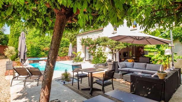 Un espace patio avec une piscine, du mobilier d’extérieur et un coin salon abrité.