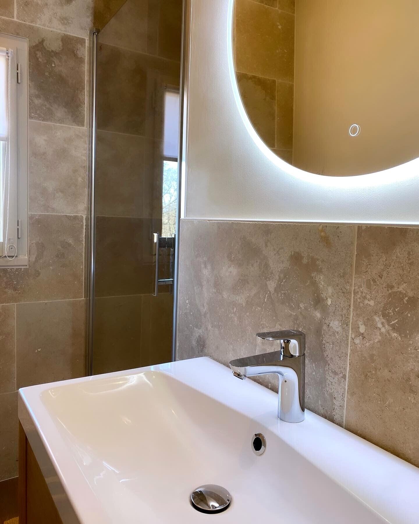 Een moderne badkamer met een groot wit wastafel, een chromen kraan en een douchecabine met glazen wanden.