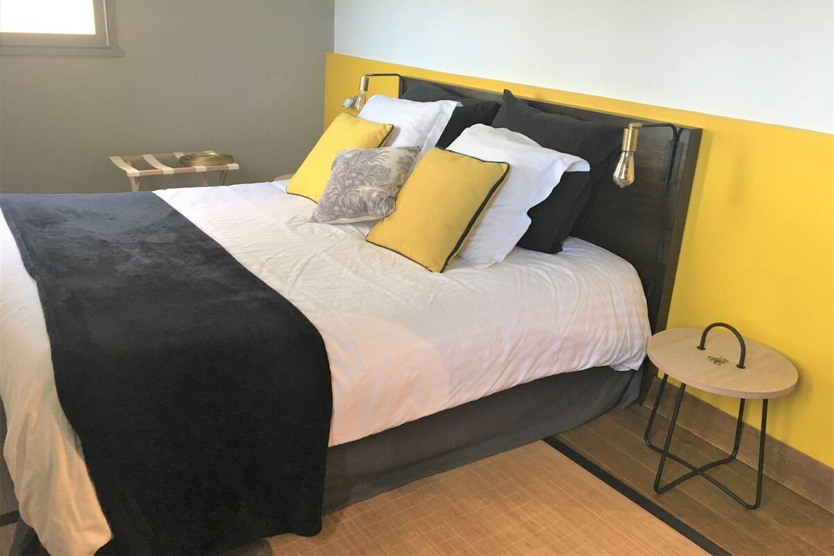 A bed with a black headboard, white bedding, and multiple pillows in yellow and gray.