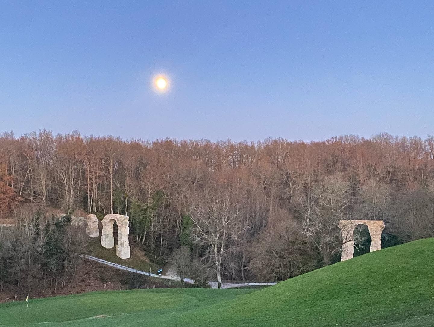 A historic stone arch bridge in a rural setting with a clear sky and a full moon.