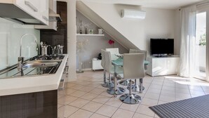 Une cuisine moderne dotée d’une cuisinière intégrée, un coin repas avec une table et des chaises en verre, un téléviseur à écran plat et un escalier menant à un niveau supérieur.