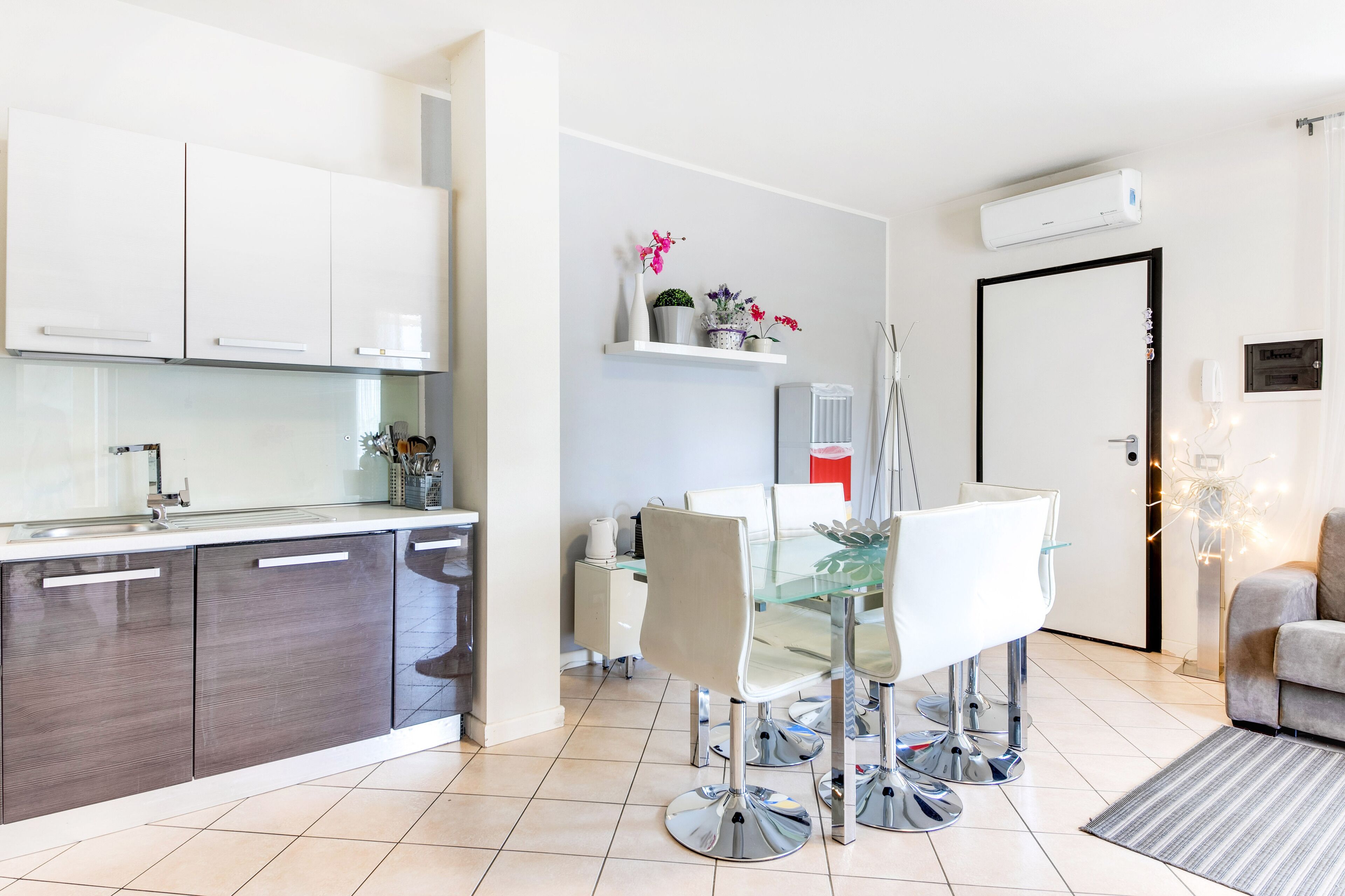 A modern kitchen with white cabinets, a glass dining table, and a coffee machine.