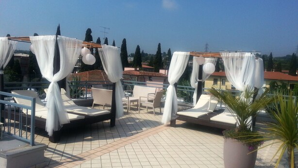 Une terrasse sur le toit, dotée de quatre espaces aménagés avec des auvents blancs, chacun comprenant une chaise et une petite table. La terrasse est recouverte de carreaux et entourée d’une rambarde en métal.
