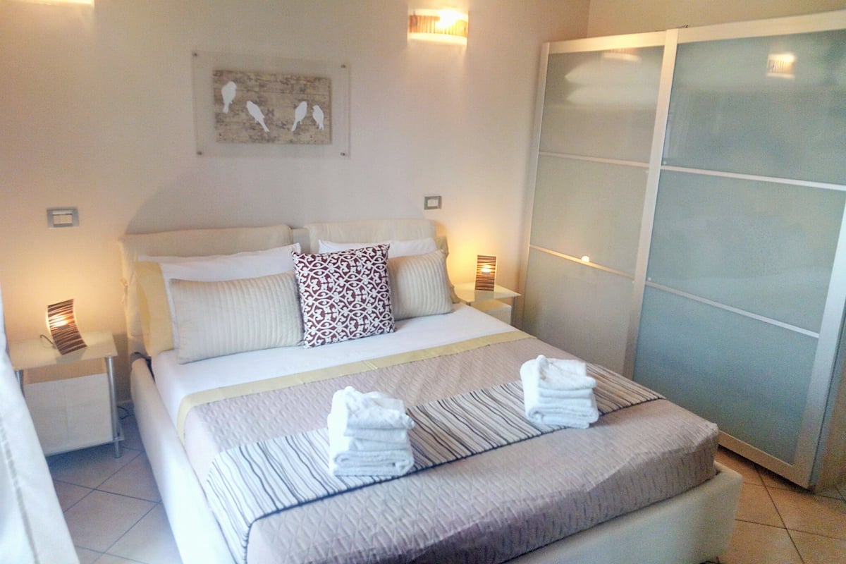 A hotel room with a bed, two bedside tables, a nightstand, a wall-mounted artwork, and a sliding door closet.