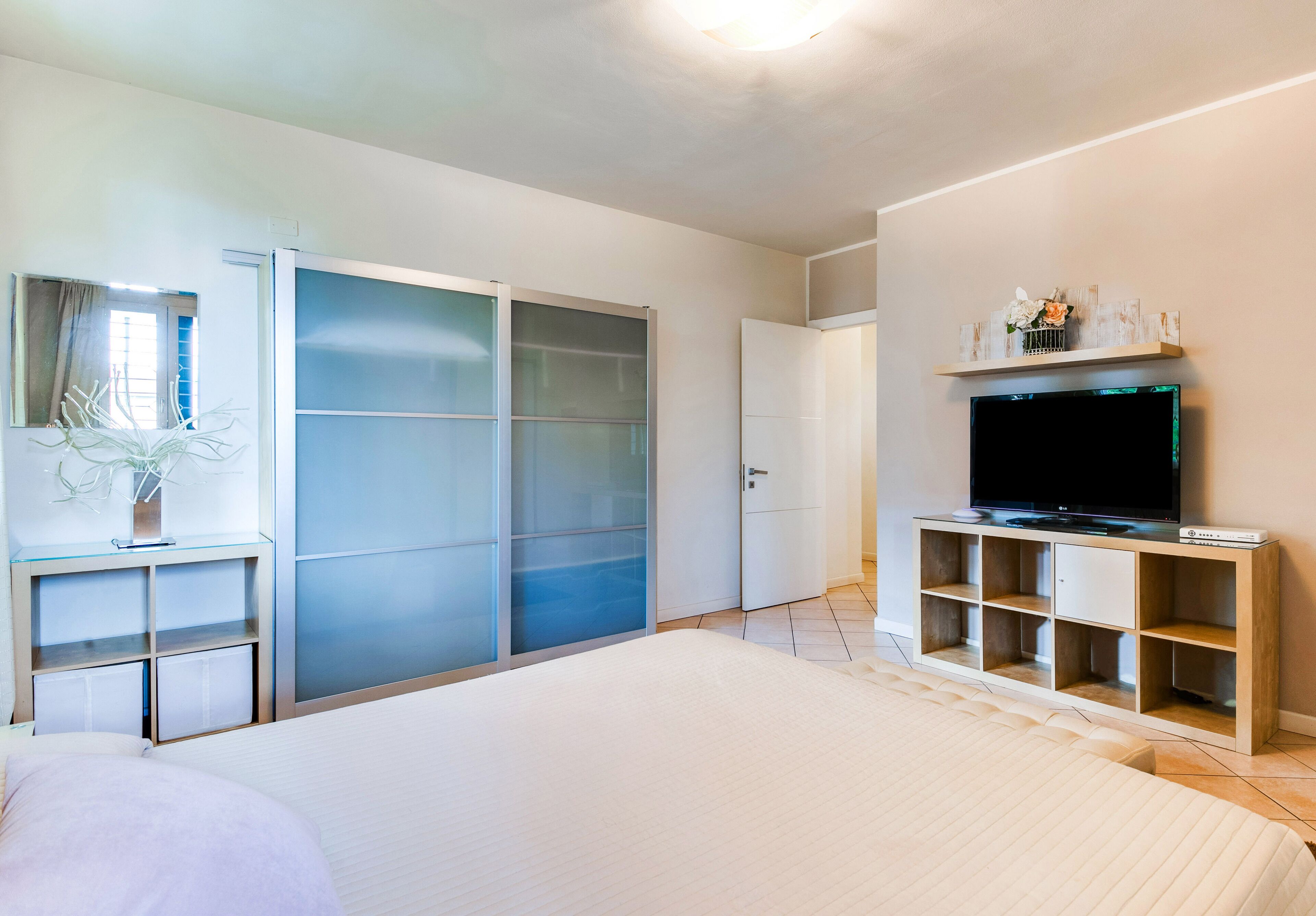 A bedroom with a bed, a TV, a wardrobe, and a shelf with decorative items.