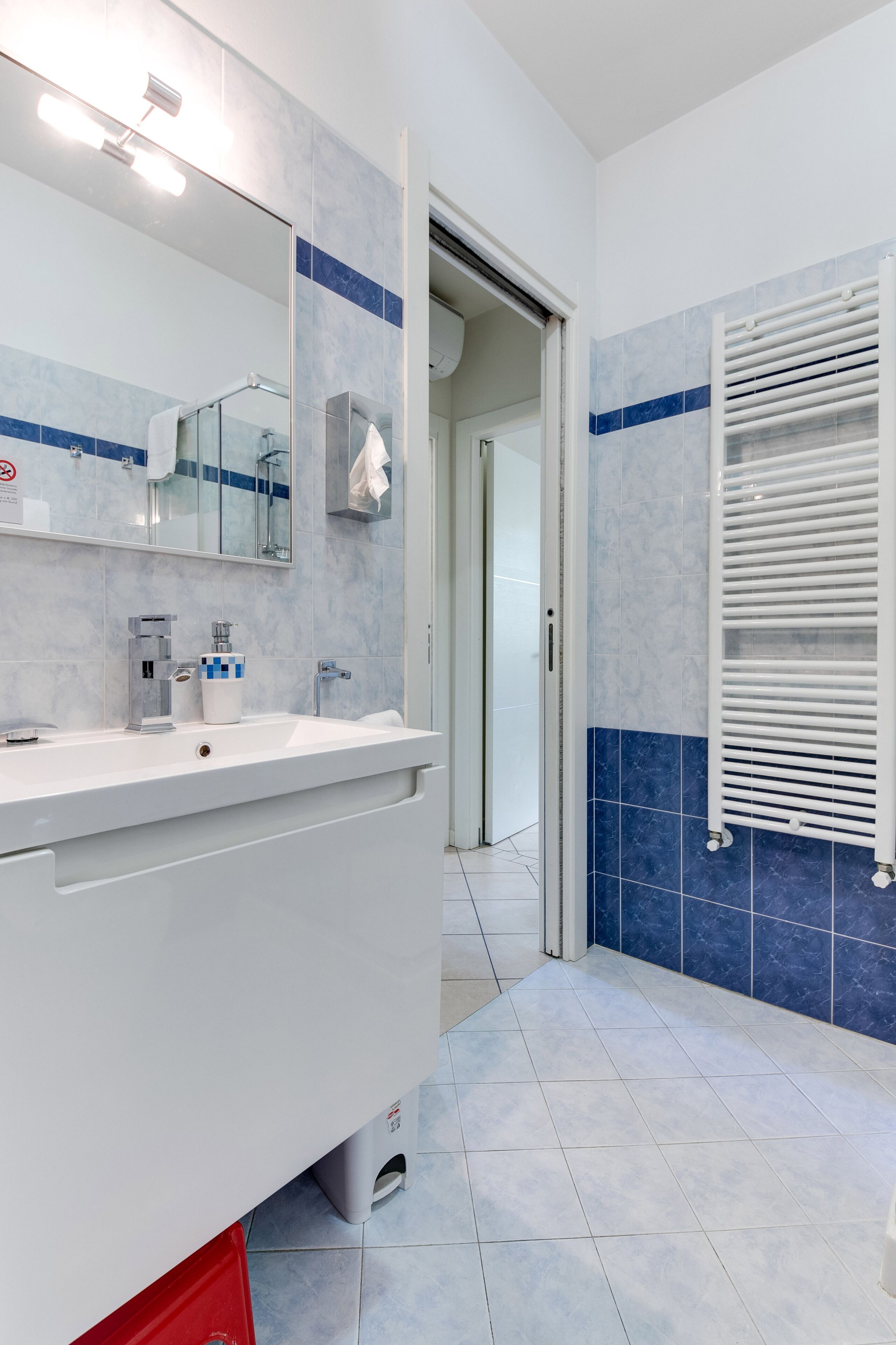 Un baño moderno con tocador blanco, un espejo grande y un perchero para toallas.
