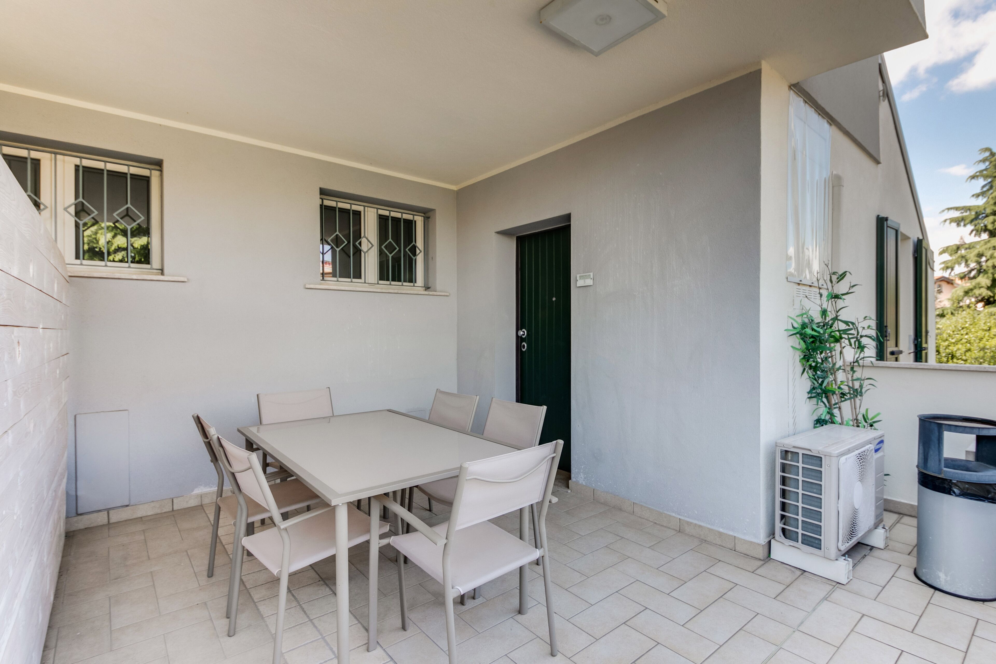 Een terras met een tafel, stoelen, een deur, een airconditioning en een vuilnisbak.