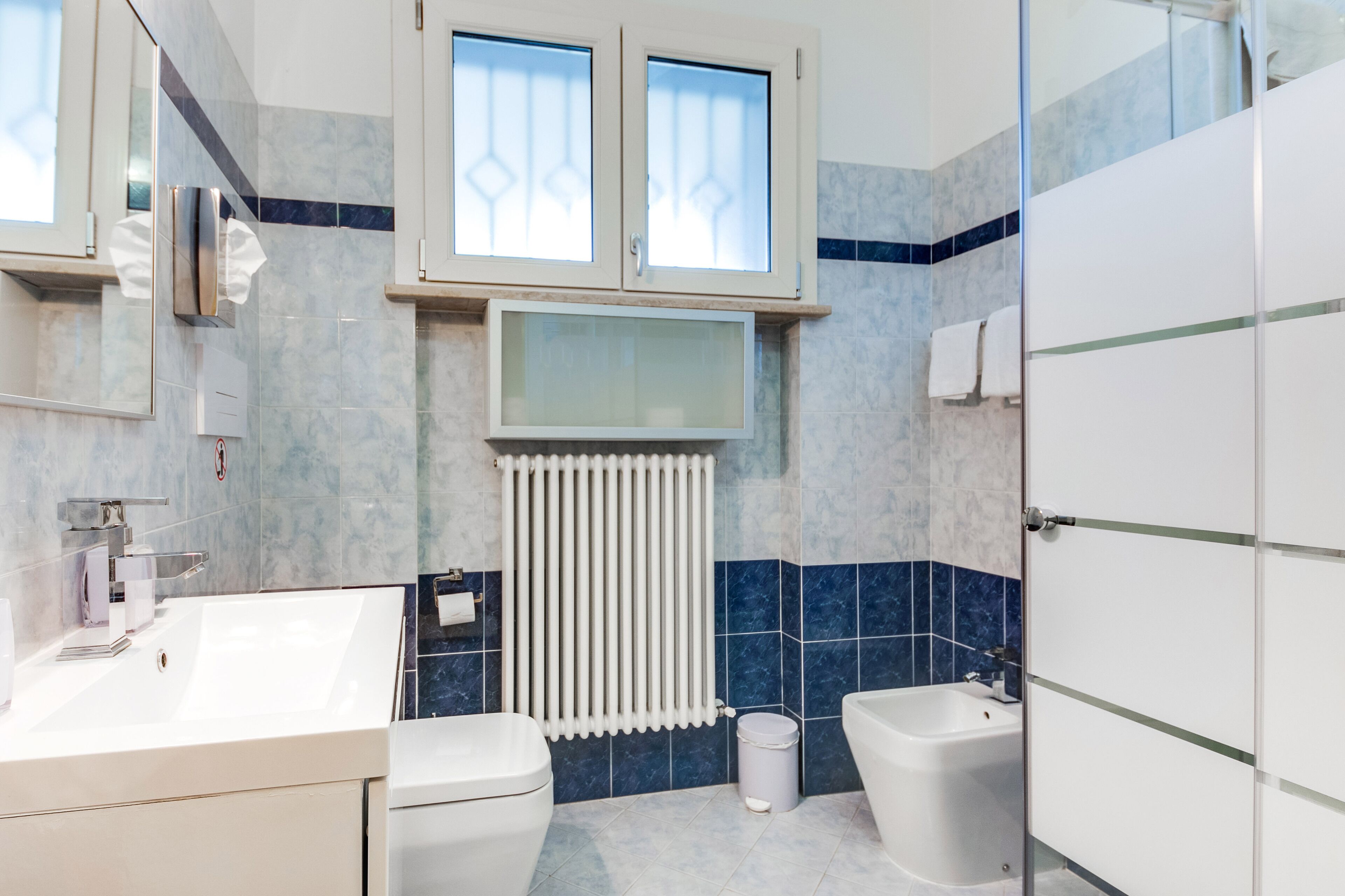 Ein modernes Badezimmer mit einem weißen Waschbecken, zwei Toiletten, einer Badewanne und einem Fenster über dem Waschbecken.