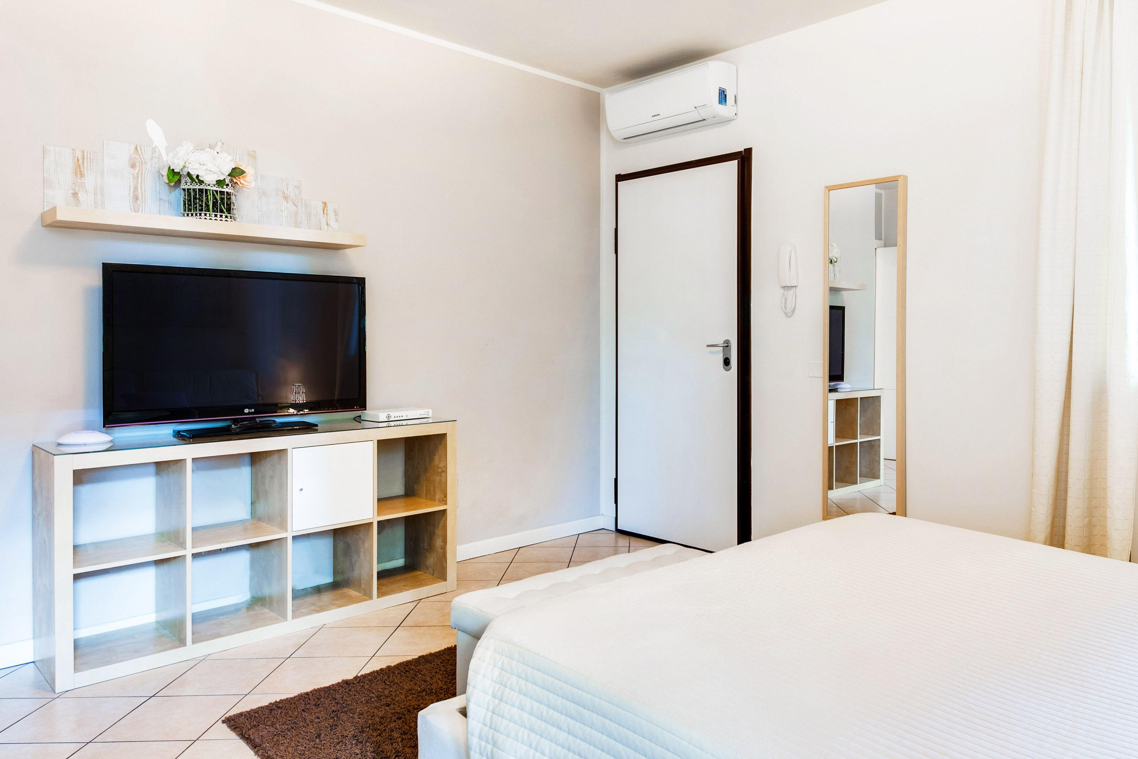 A bedroom with a bed, a TV on a stand, a wardrobe, and an air conditioning unit.