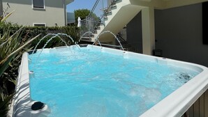 Une piscine avec un jacuzzi, entourée d’une terrasse en bois et d’une rambarde en métal.