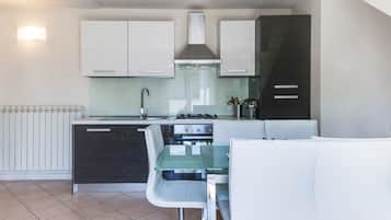 A compact kitchen with white cabinets, a gas stove, and a glass dining table.