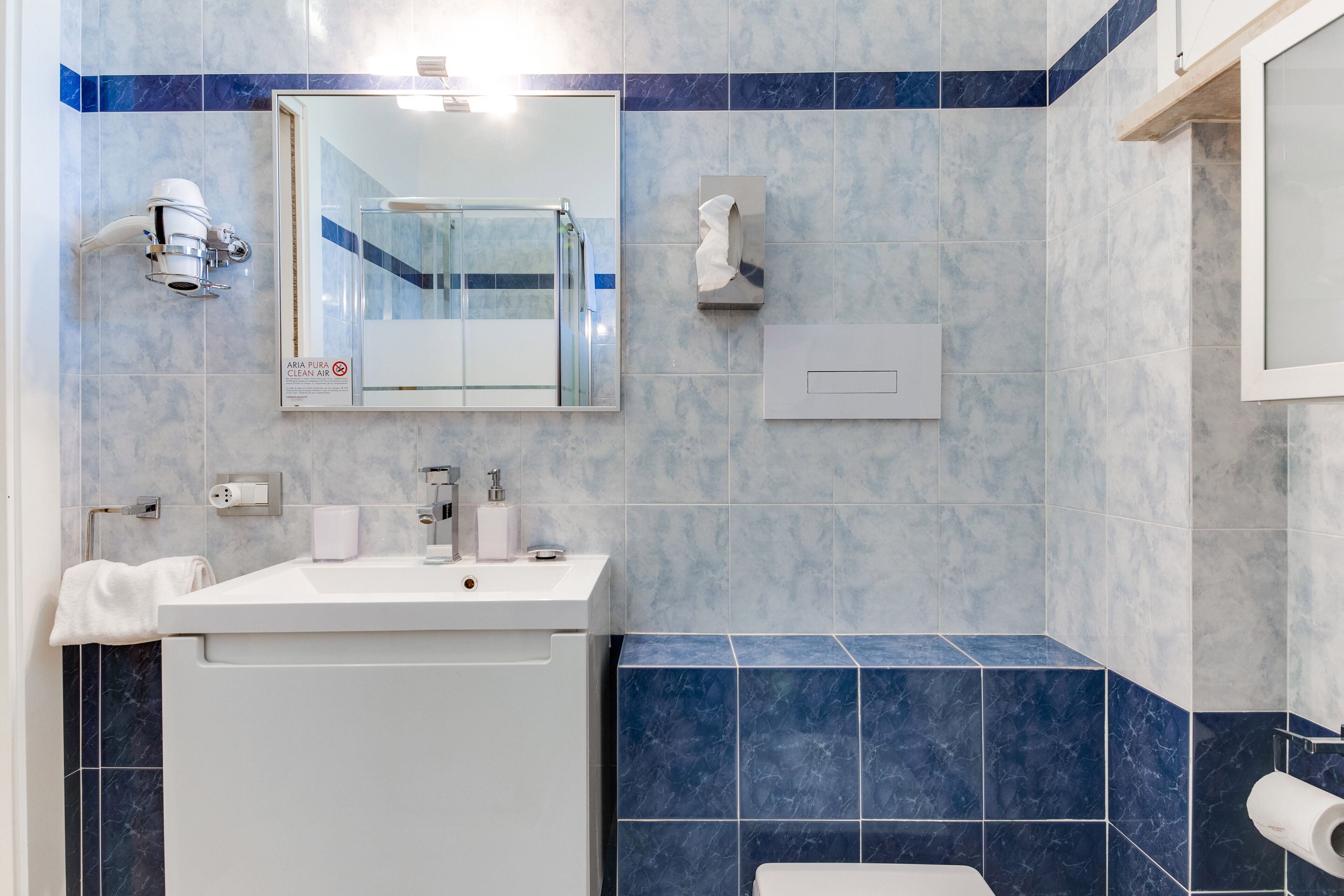 Une salle de bain moderne avec un lavabo blanc, un miroir et des murs recouverts de carreaux bleus.