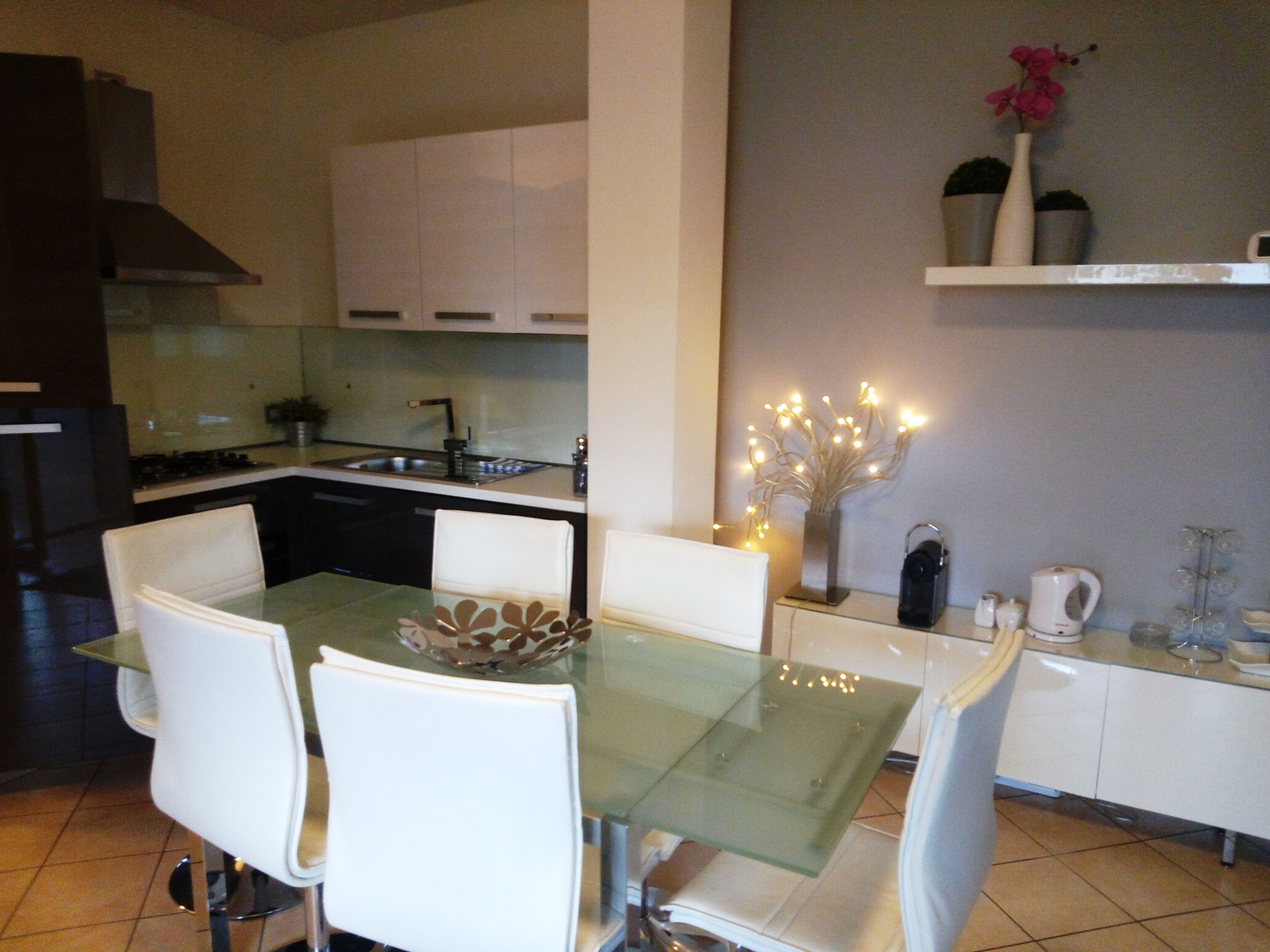 A modern kitchen with white cabinets, a glass dining table, and white chairs.