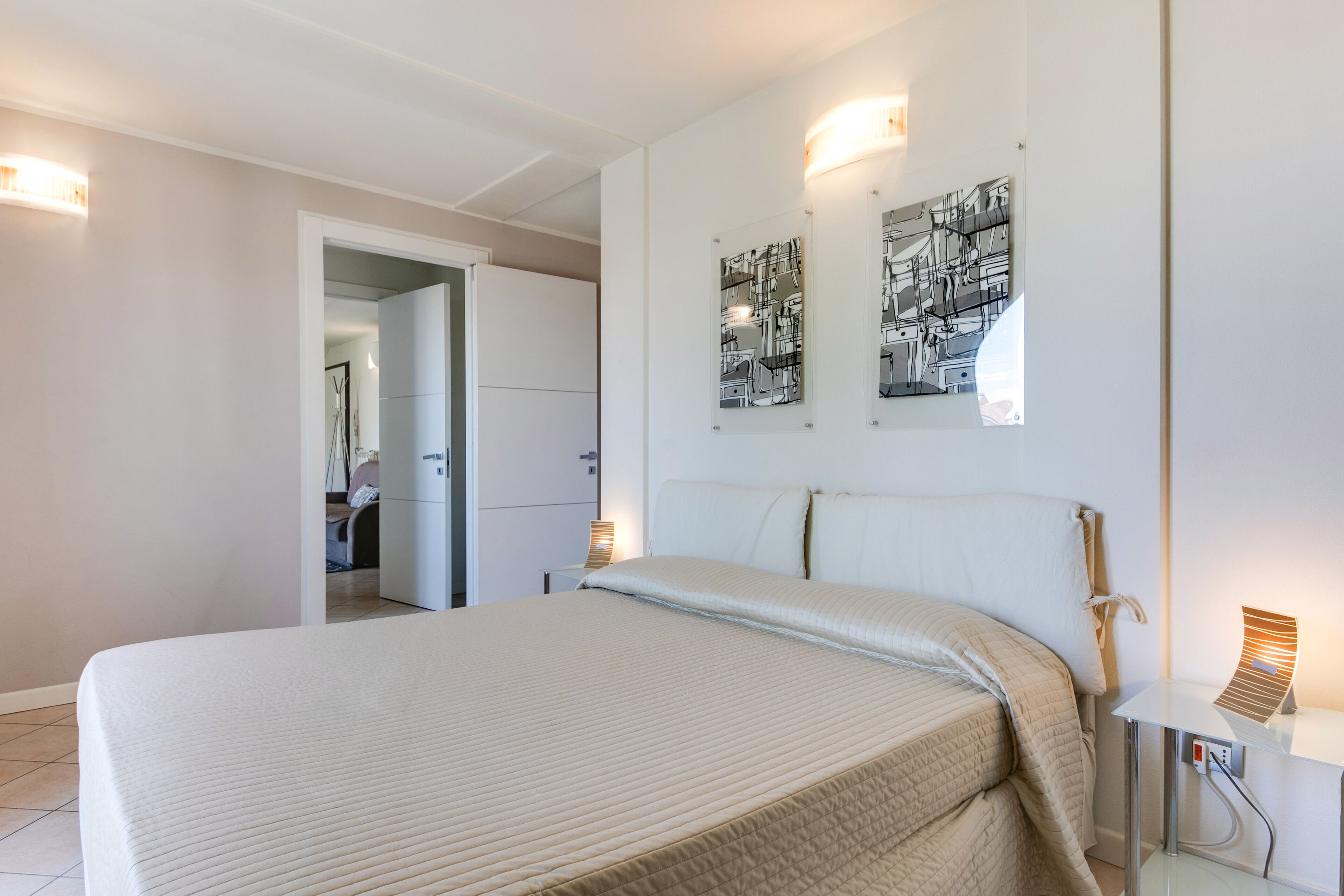 Un dormitorio con una cama, una mesita de noche con lámpara y dos obras de arte colgadas en la pared.