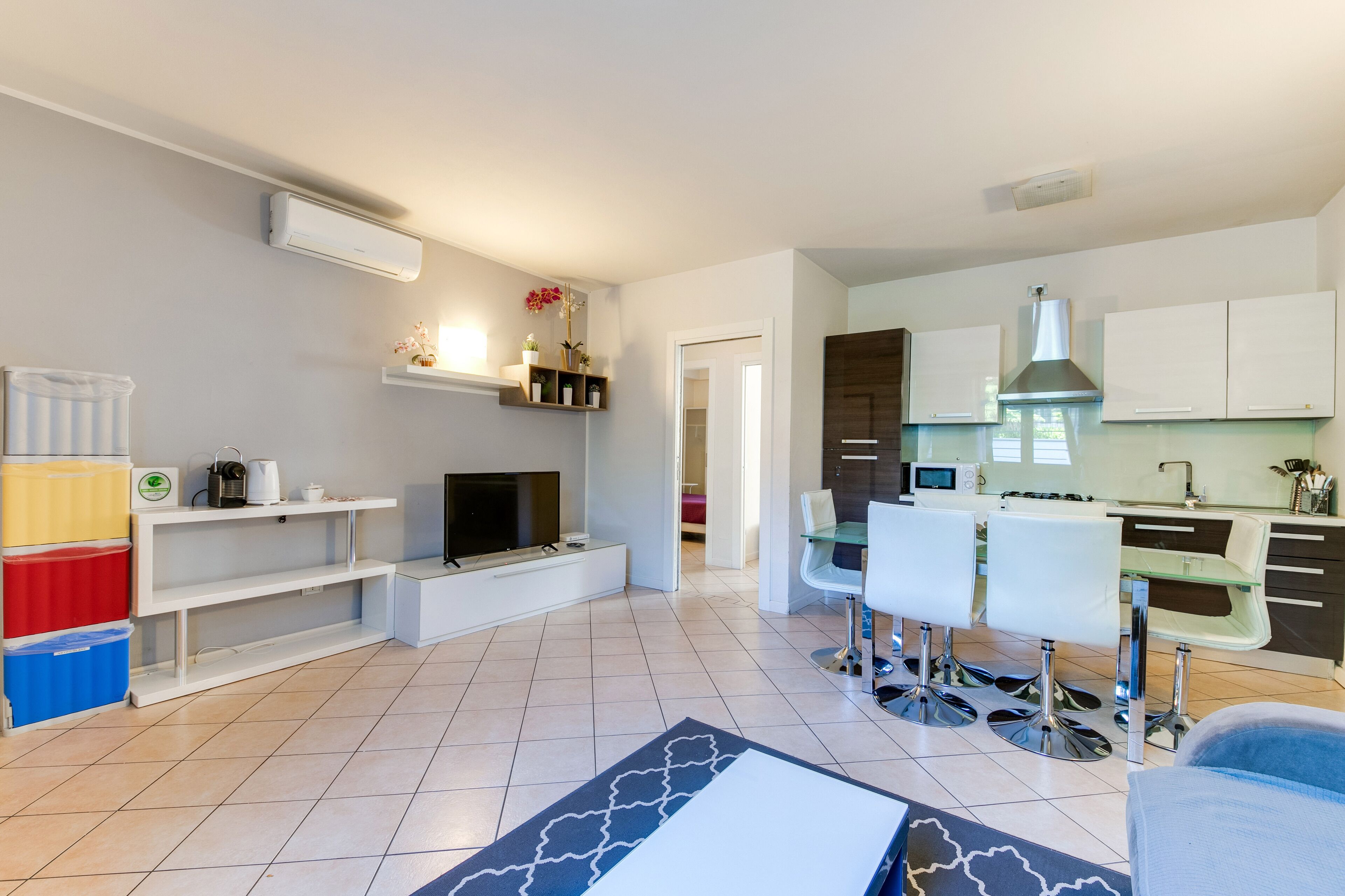 A modern living room with a TV, seating area, and a kitchen in the background.
