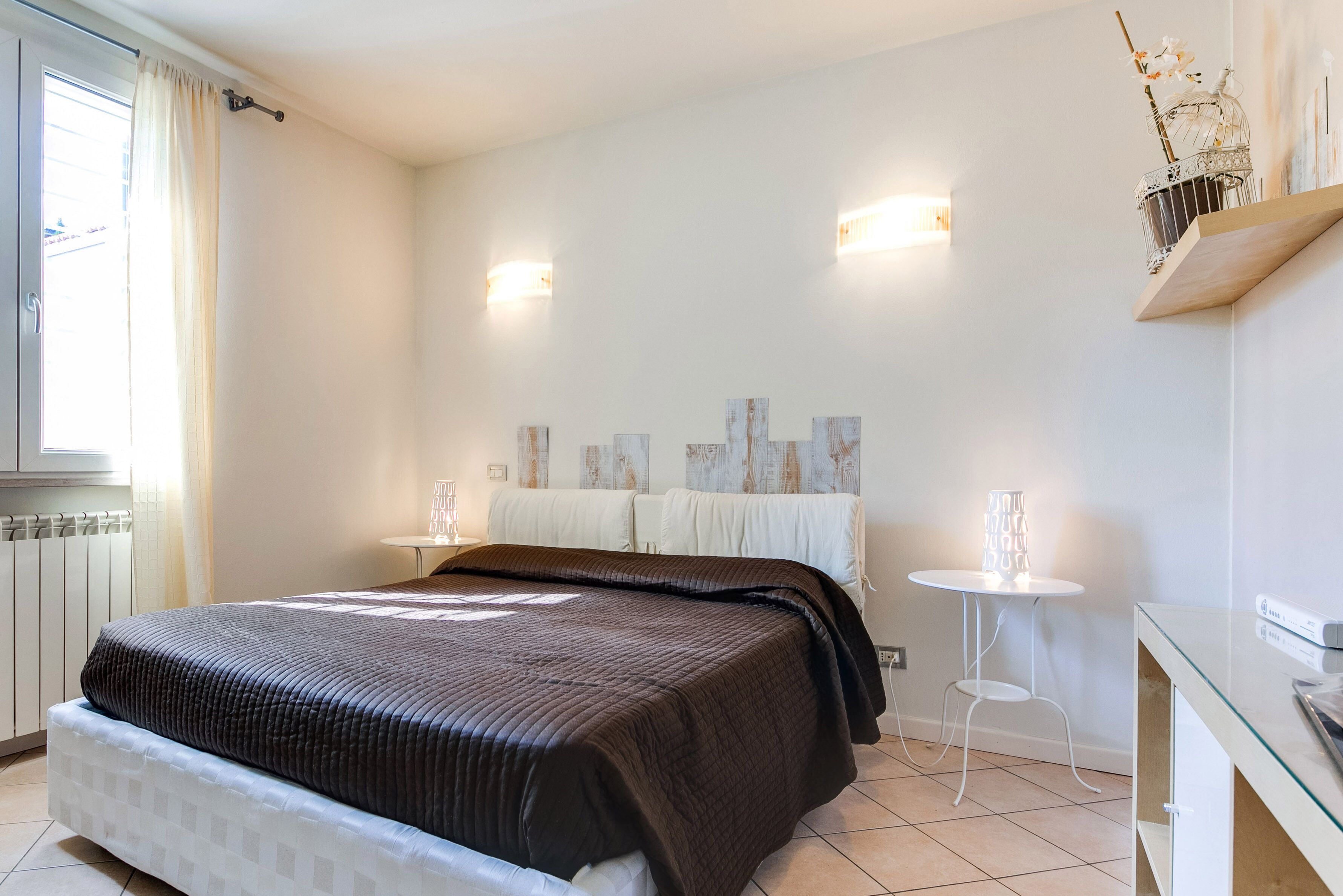 A bedroom with a bed, bedside tables, a small table, and wall-mounted lights.
