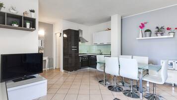 A modern kitchen with white cabinets, a black stove, and a dining area with white chairs and a glass table.