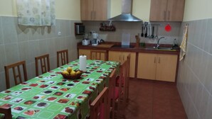 Una cucina compatta con mobili in legno, un tavolo da pranzo con tovaglia a fantasia di frutta ed elettrodomestici essenziali.