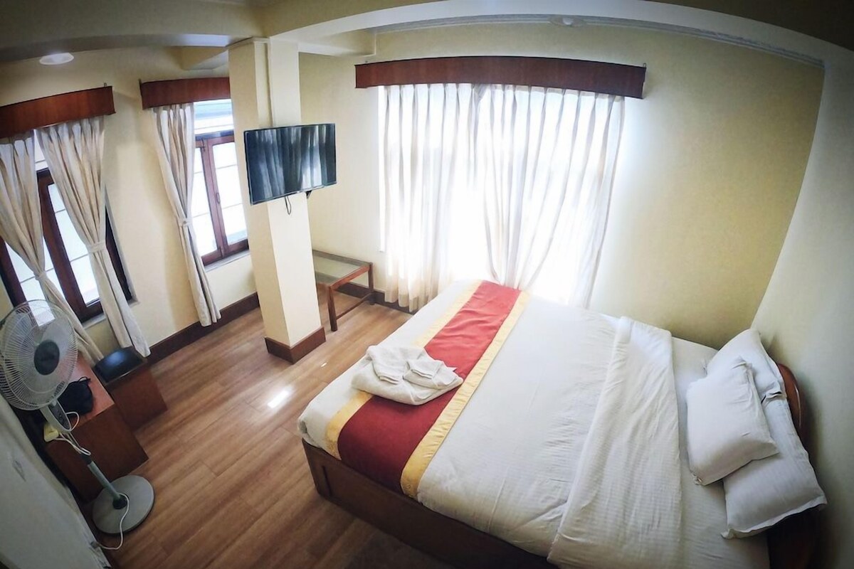 Una habitación de hotel con cama, televisión, ventilador y cortinas.