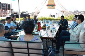 A group of people seated around a table with water bottles and fruits, in an outdoor setting with a large white structure in the background. - Hotel Bodhiz (Kathmandu)
