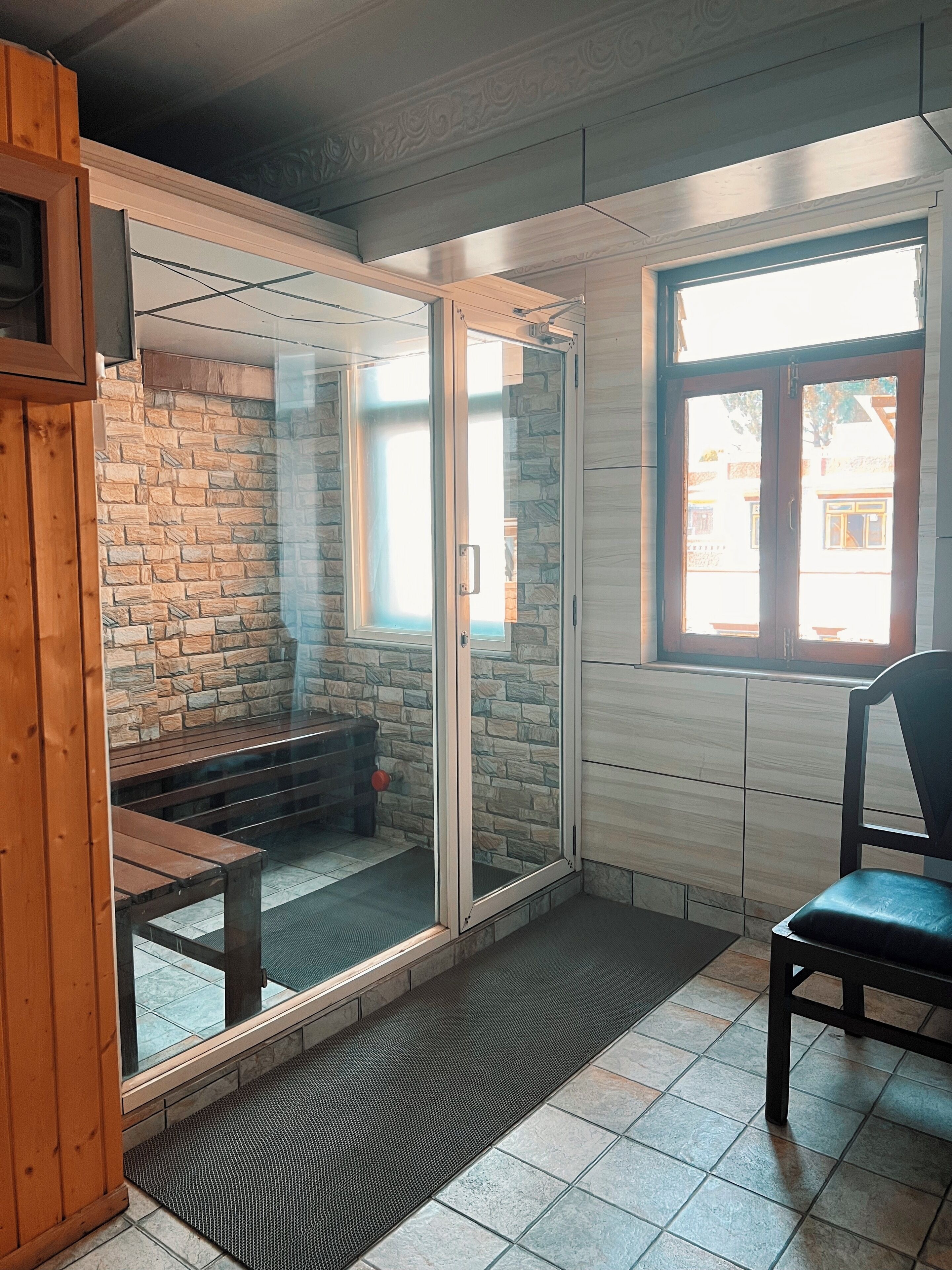 Una habitación con pared de piedra, un banco de madera, una puerta de cristal y una ventana.