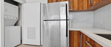 Une cuisine équipée d’un réfrigérateur en acier inoxydable, de meubles de rangement en bois, d’un plan de travail blanc et d’un four encastré.