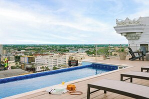 Une piscine sur le toit offrant une vue sur la ville, des chaises longues et une fontaine décorative.