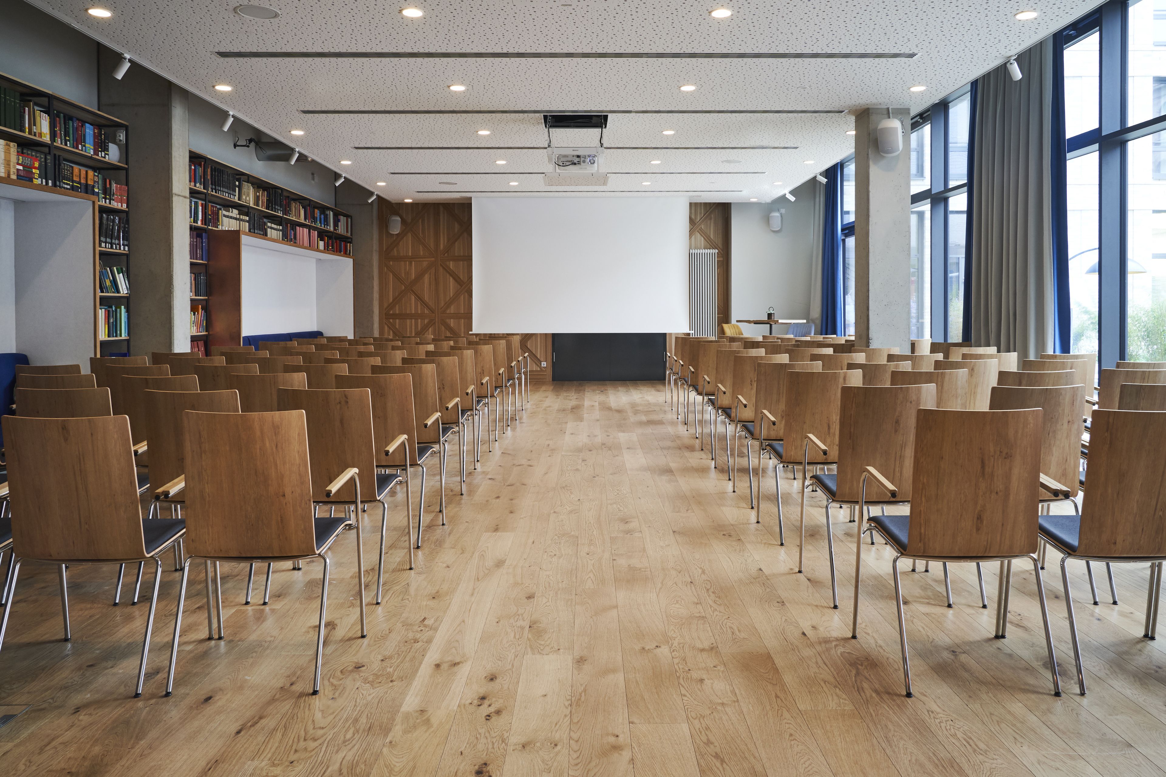 Une salle de conférence avec des rangées de chaises, un écran de projection et des étagères à livres.