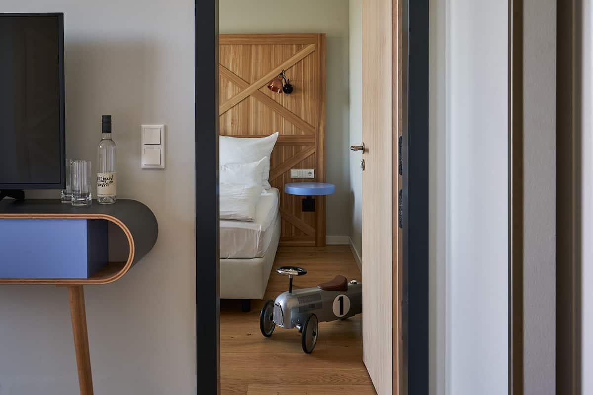 A modern hotel room with a wooden headboard, a bed, a small round table, and a toy car.