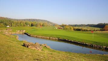 A golf course with a pond, green fields, and a distant hill.