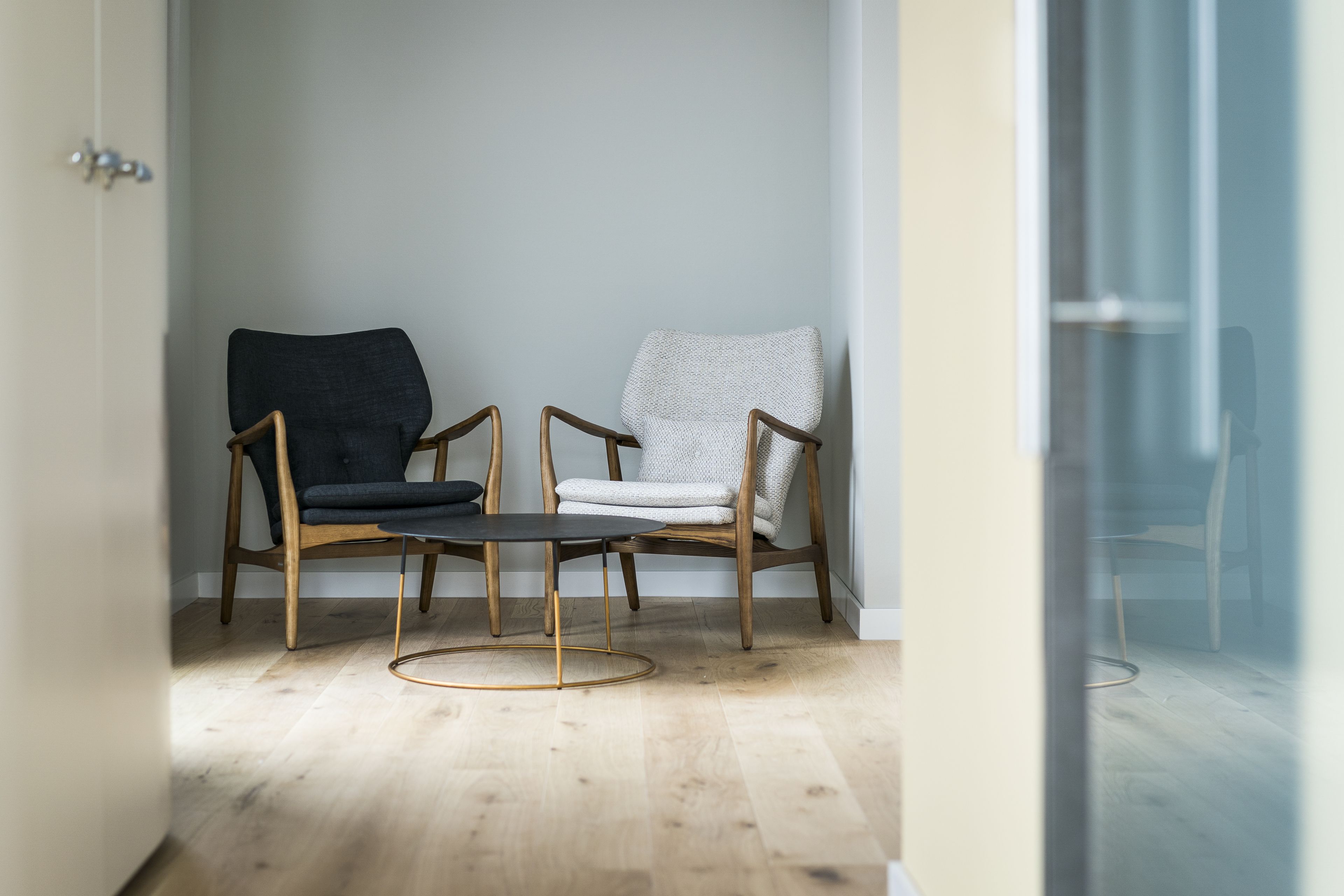 A room with two wooden chairs and a small round table, a door, and a glass partition.