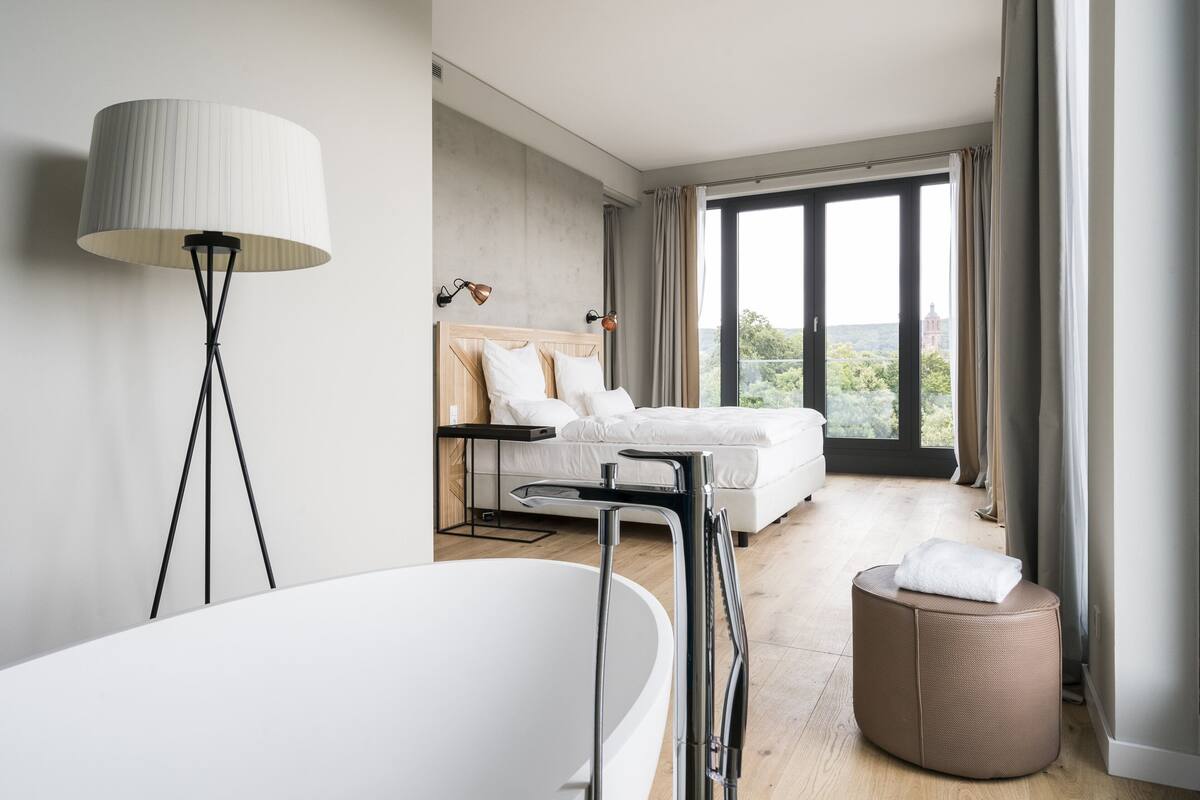 A modern bedroom with a large bed, a standing bathtub, and a view of the outdoors.