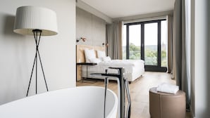 A modern bedroom with a large bed, a standing bathtub, and a view of the outdoors.