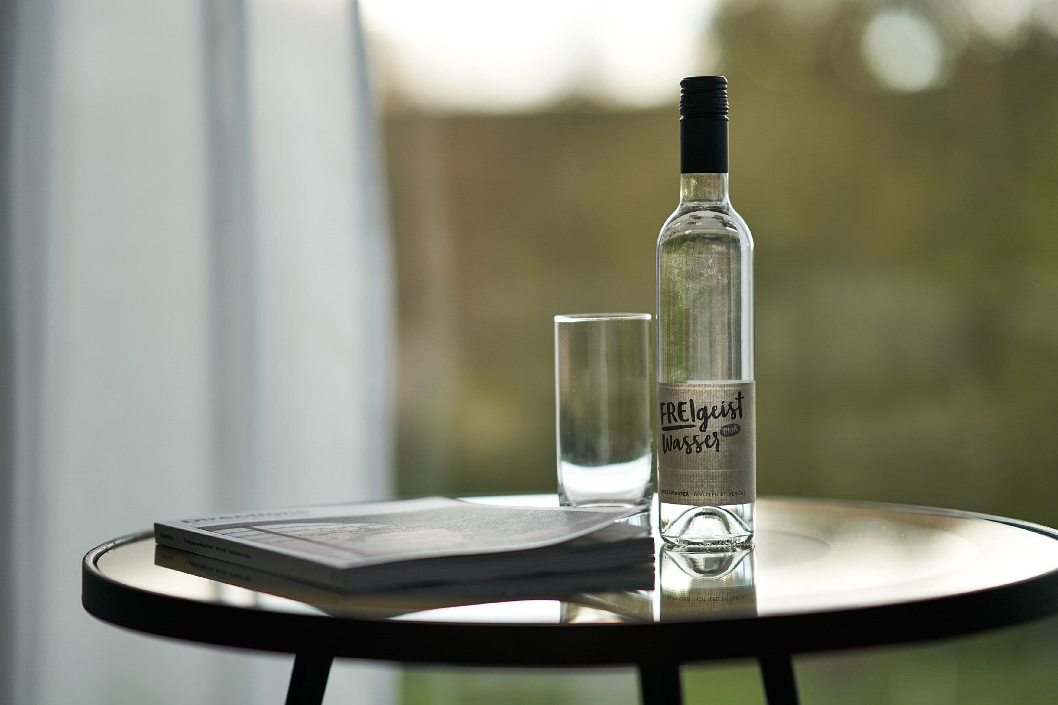 A bottle of Freigast Wasser and a glass on a round table with a book.