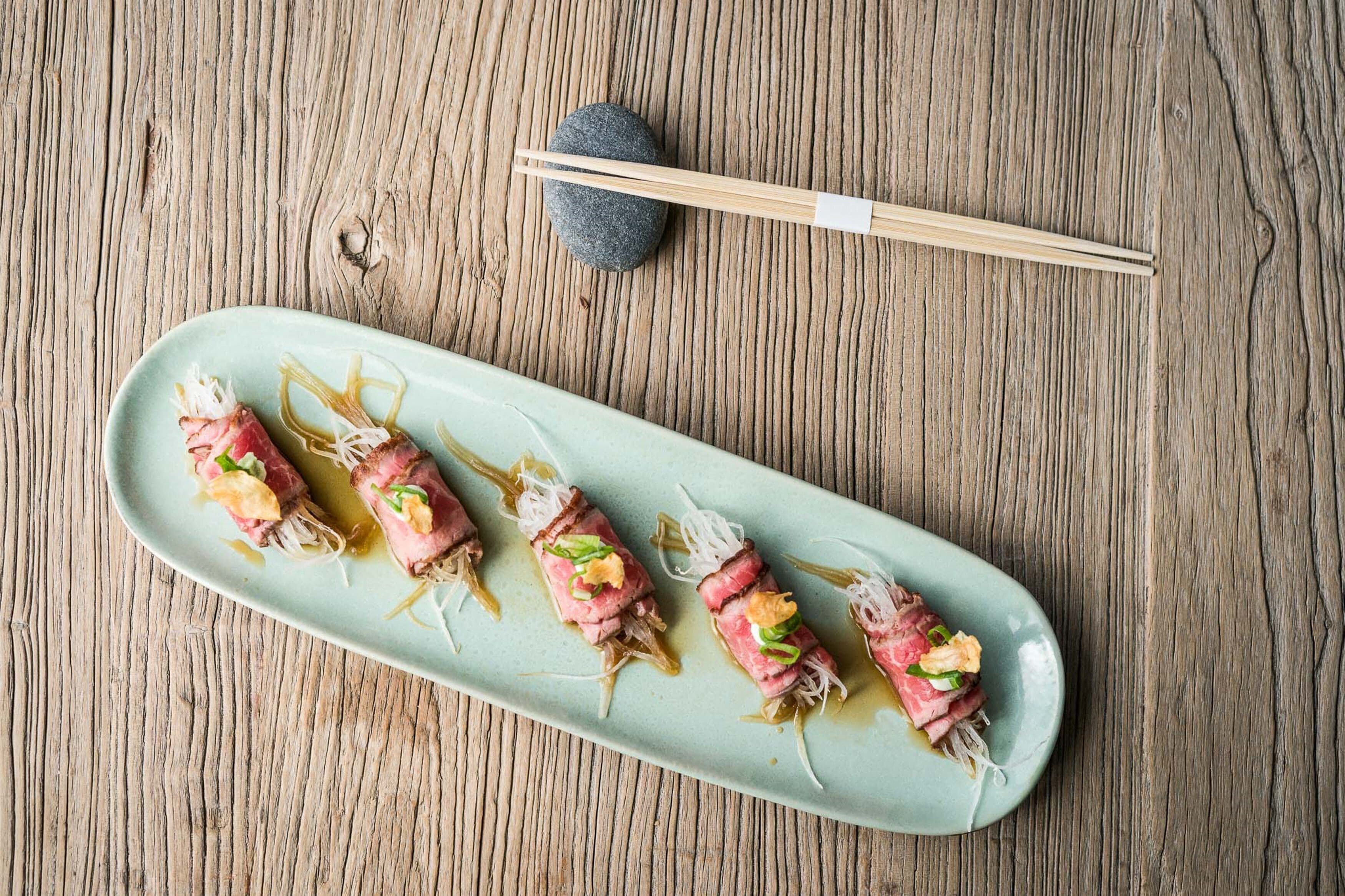 A plate of sushi with chopsticks and a stone on a wooden table.