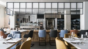 A modern restaurant with a bar area, high stools, and a kitchen in the background.