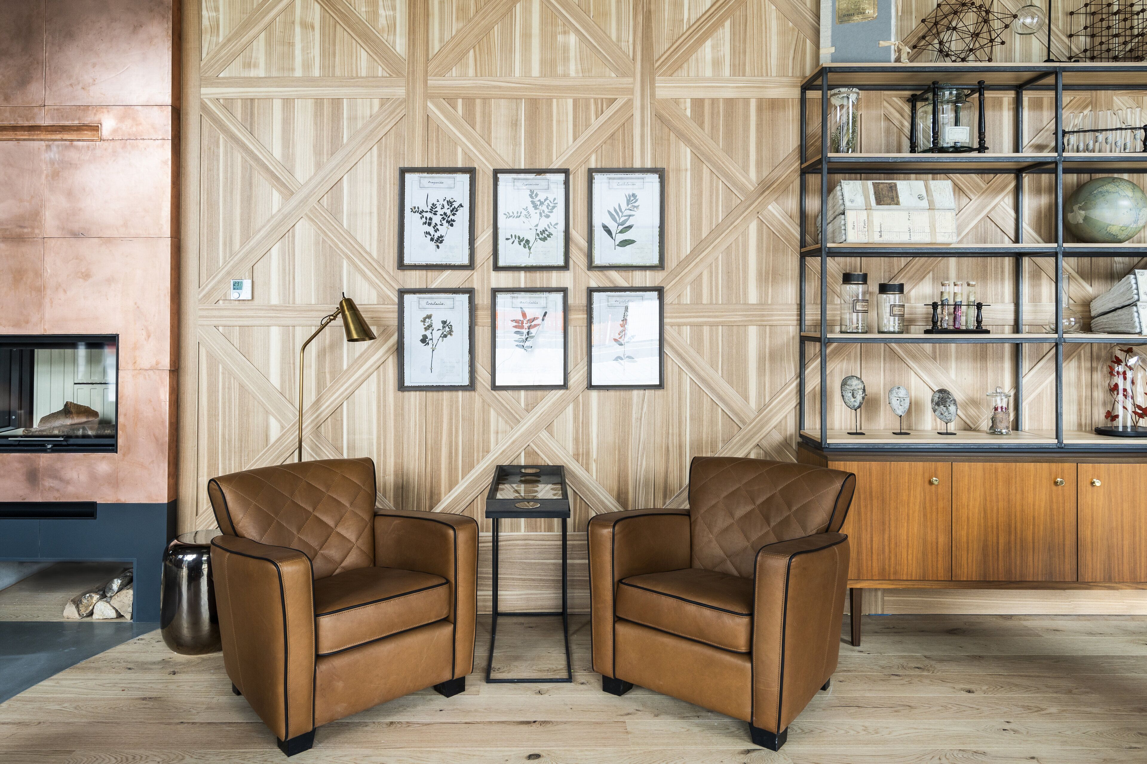 Une pièce comprenant deux fauteuils en cuir marron, une petite table, une bibliothèque remplie de divers objets et, au mur, des reproductions encadrées de planches botaniques.