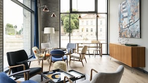 A modern living room with large windows, a variety of seating options, and a wooden cabinet.