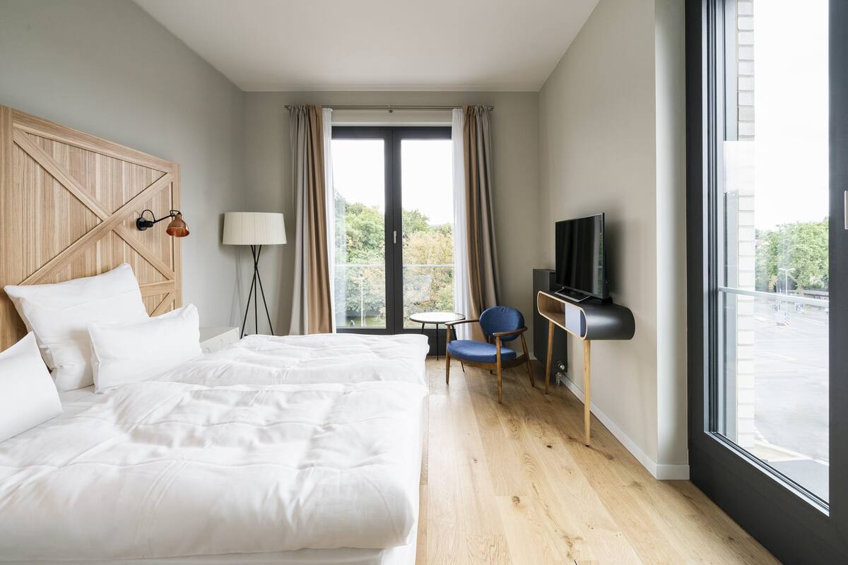 A hotel room with a large bed, a desk with a chair, a TV, and a window with curtains.