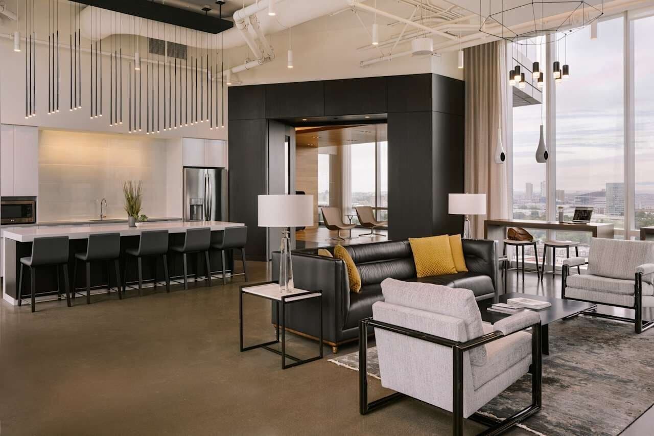 Un salon moderne comprenant un canapé, des fauteuils, une table basse et un coin bar avec des tabourets.