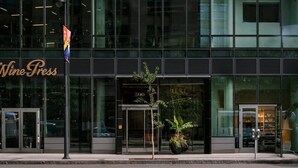Un edificio moderno con fachada de vidrio, una bandera y un letrero que dice 'Wine Press'.